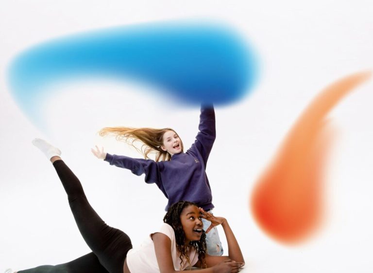 Zwei Kinder toben vor einem farbigen Schwung aus Blau und Orange